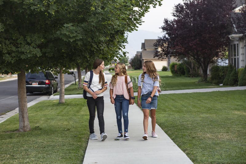 Group of young female friends and students talking together as they walk home school for the day. Kids walking to school with lots of copy space. Education and social concept photo. Group of young female friends and students talking together as they walk home school for the day. Kids walking to school with lots of copy space. Education and social concept photo