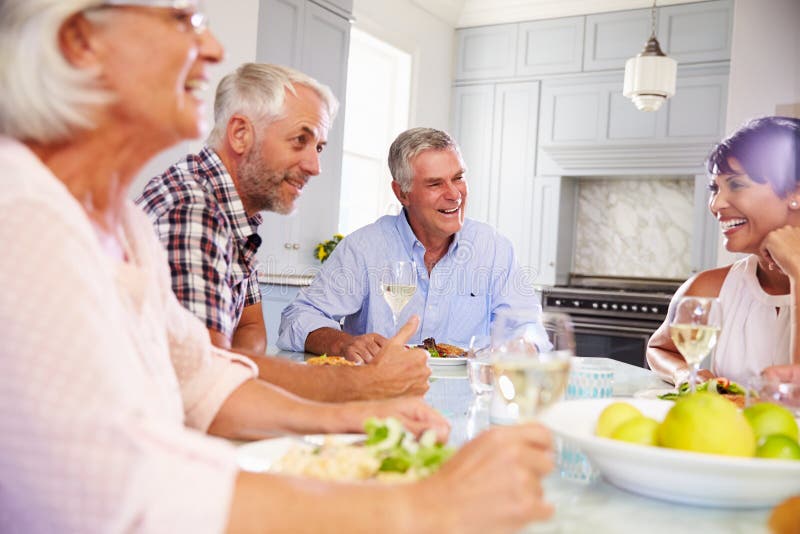 Grupo de amigos maduros que disfrutan de la comida en casa junto imagenes de archivo Grupo de amigos maduros que disfrutan de la comida en casa junto imagenes de archivo