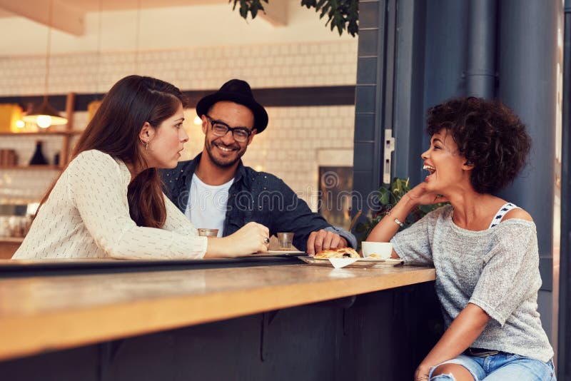 Portrait of a young group of friends talking in a cafe. Young men and women sitting at cafe table and talking. Portrait of a young group of friends talking in a cafe. Young men and women sitting at cafe table and talking.