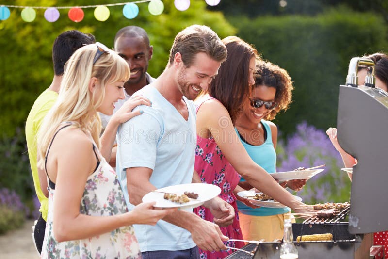 Group Of Friends Having Outdoor Barbeque At Home In Garden Serving Food. Group Of Friends Having Outdoor Barbeque At Home In Garden Serving Food