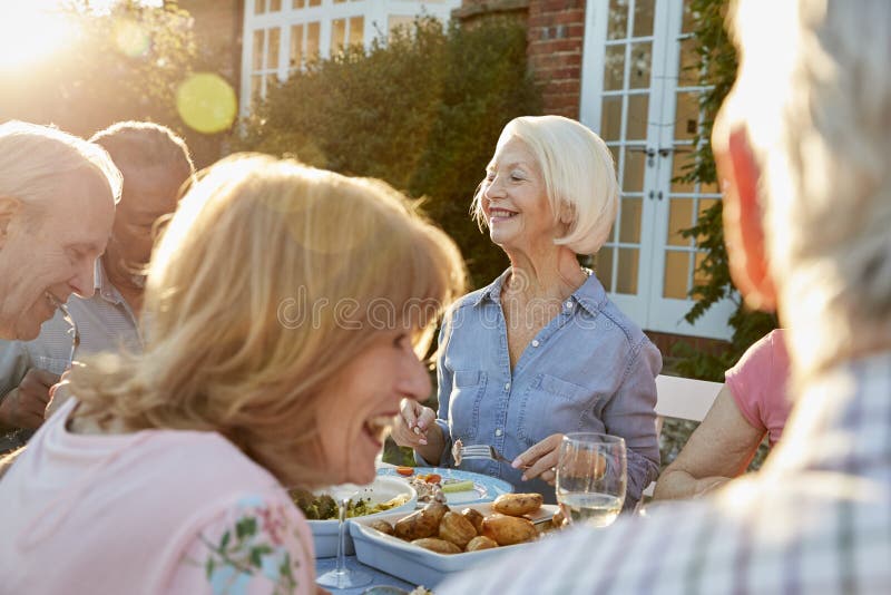 Grupo de amigos superiores que apreciam o partido de jantar exterior em casa imagem de stock Grupo de amigos superiores que apreciam o partido de jantar exterior em casa imagem de stock