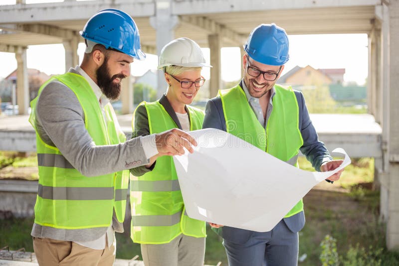 Grupo de arquitetos ou de sócios comerciais que discutem plantas baixas em um canteiro de obras imagens de stock Grupo de arquitetos ou de sócios comerciais que discutem plantas baixas em um canteiro de obras imagens de stock