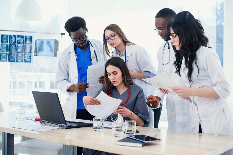 Grupo de doctores nacionales multi jovenes durante el trabajo con el ordenador port?til en la sala de conferencias imágenes de archivo libres de regalías Grupo de doctores nacionales multi jovenes durante el trabajo con el ordenador port?til en la sala de conferencias imágenes de archivo libres de regalías