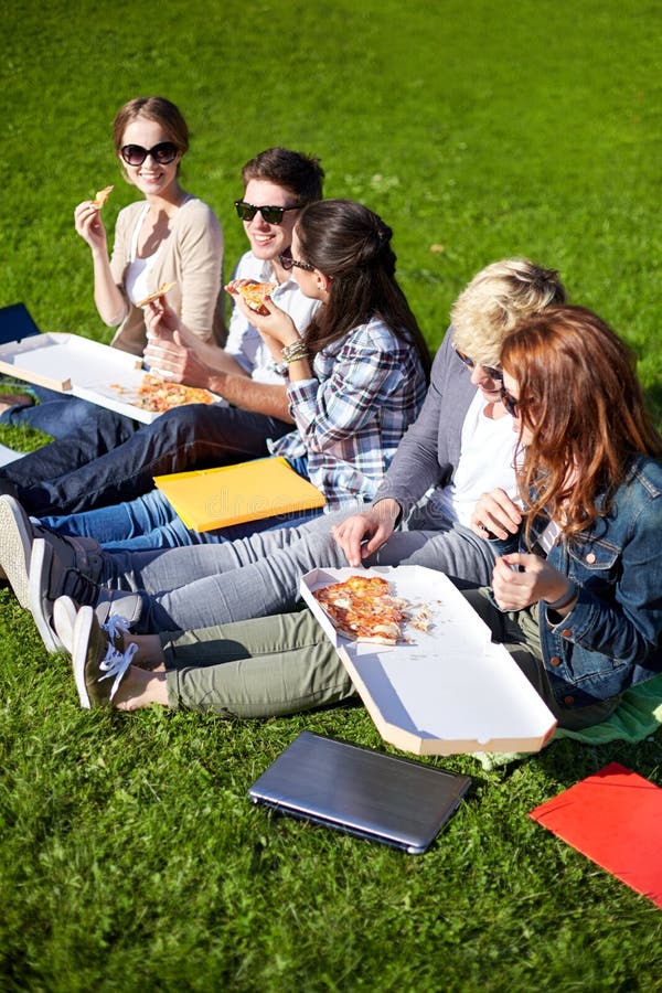 Grupo de estudantes adolescentes que comem a pizza na grama fotografia de stock Grupo de estudantes adolescentes que comem a pizza na grama fotografia de stock