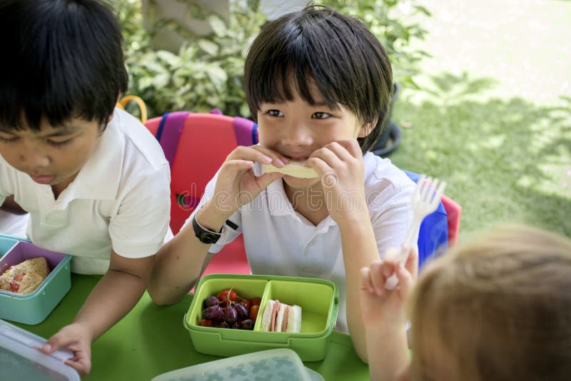 Grupo de estudantes do jardim de infância que comem a pausa para o almoço do alimento junto imagens de stock Grupo de estudantes do jardim de infância que comem a pausa para o almoço do alimento junto imagens de stock