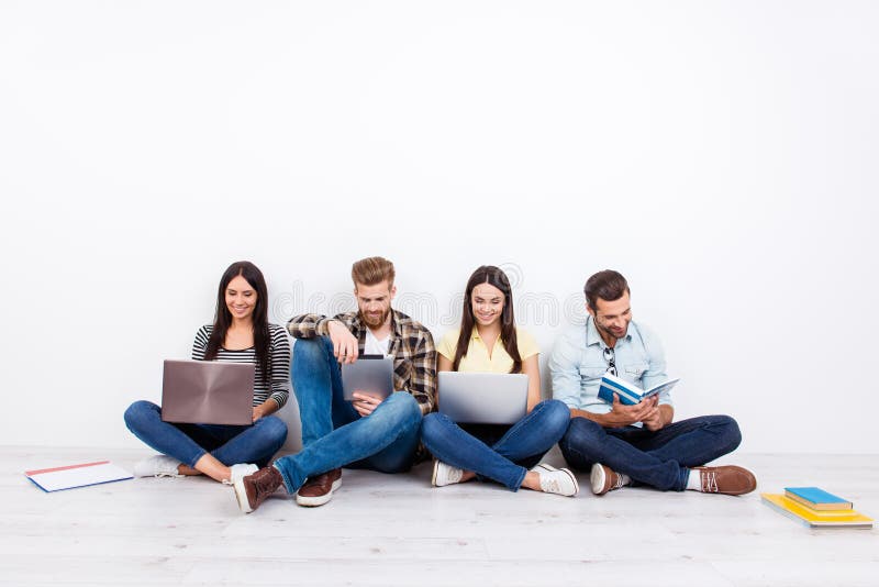 Grupo de estudantes de sorriso amigáveis que sentam-se no assoalho e no usin imagem de stock royalty free Grupo de estudantes de sorriso amigáveis que sentam-se no assoalho e no usin imagem de stock royalty free