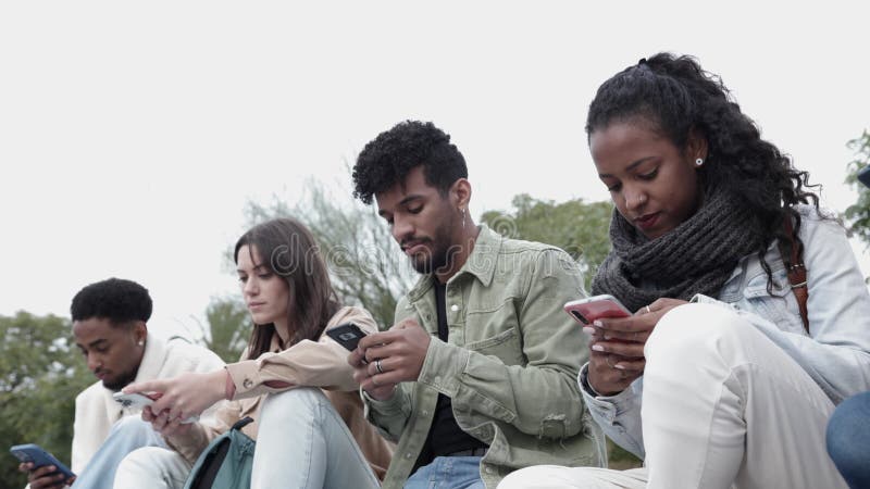 Grupo de estudiantes adolescentes que usan teléfonos inteligentes mientras están sentados al aire libre