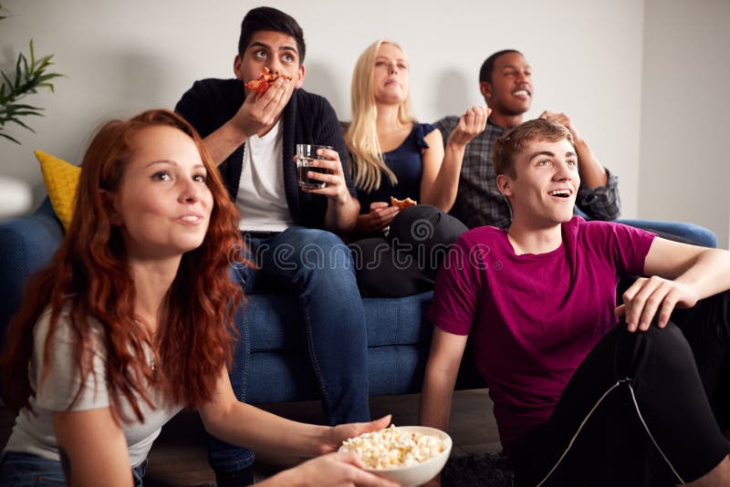 Grupo De Estudiantes Universitarios En Casa Compartida Viendo La Televisión Y Comiendo Palomitas fotografía de archivo