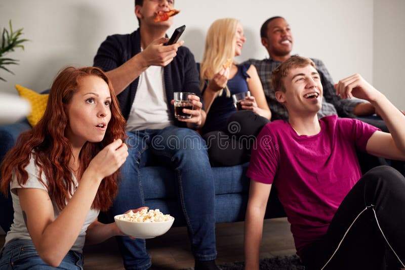 Grupo De Estudiantes Universitarios En Casa Compartida Viendo La Televisión Y Comiendo Palomitas foto de archivo libre de regalías