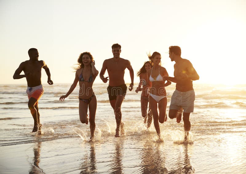 Grupo de funcionamiento de los amigos a través de ondas junto el vacaciones de la playa fotografía de archivo libre de regalías Grupo de funcionamiento de los amigos a través de ondas junto el vacaciones de la playa fotografía de archivo libre de regalías
