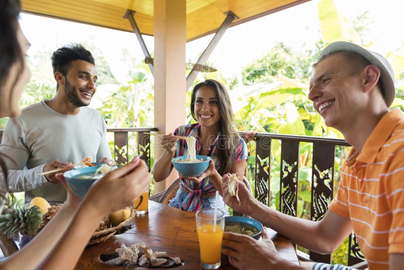 Grupo de gente joven que habla mientras que come a los amigos asiáticos tradicionales de la comida de la sopa de tallarines que c imágenes de archivo libres de regalías Grupo de gente joven que habla mientras que come a los amigos asiáticos tradicionales de la comida de la sopa de tallarines que c imágenes de archivo libres de regalías