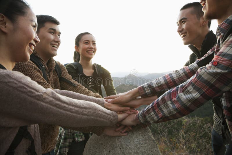 Grupo de gente joven que sonríe y que mantiene las manos unidas en la piedra imagen de archivo libre de regalías Grupo de gente joven que sonríe y que mantiene las manos unidas en la piedra imagen de archivo libre de regalías