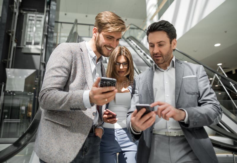 Grupo de hombres de negocios jovenes que miran las pantallas de sus smartphones imágenes de archivo libres de regalías Grupo de hombres de negocios jovenes que miran las pantallas de sus smartphones imágenes de archivo libres de regalías