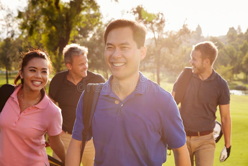 Grupo de jogadores de golfe que andam ao longo dos sacos de golfe levando do fairway fotografia de stock Grupo de jogadores de golfe que andam ao longo dos sacos de golfe levando do fairway fotografia de stock