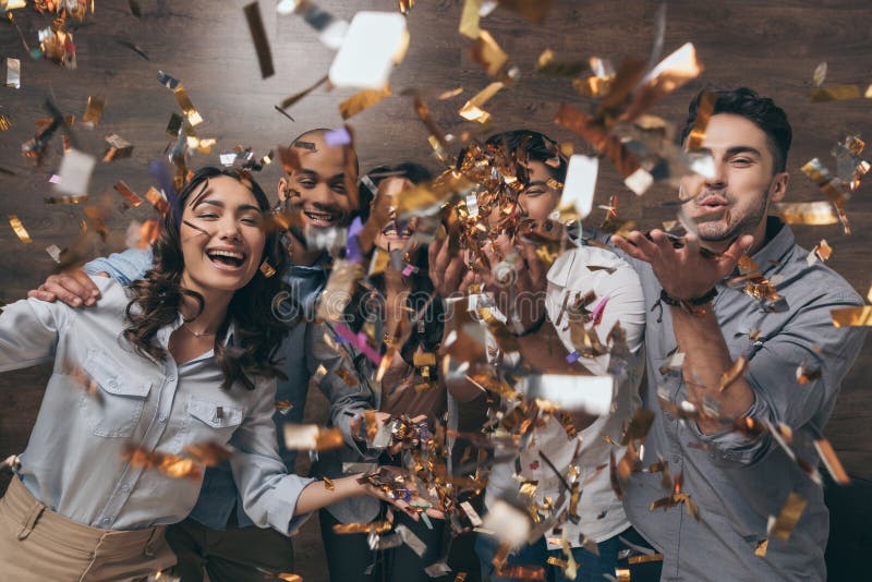Grupo de jovens alegres que estão junto e que comemoram com confetes imagem de stock Grupo de jovens alegres que estão junto e que comemoram com confetes imagem de stock
