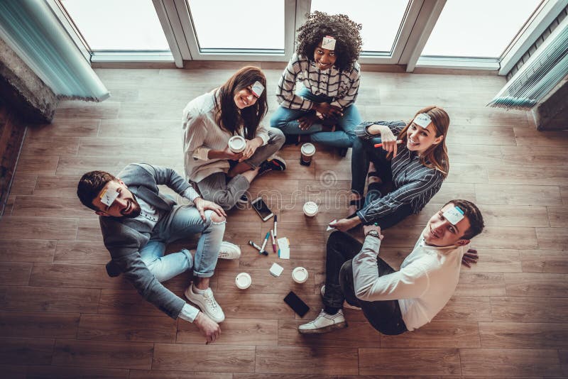 Grupo de jóvenes en la oficina jugando al juego del nombre con notas pegajosas en la frente imagen de archivo libre de regalías Grupo de jóvenes en la oficina jugando al juego del nombre con notas pegajosas en la frente imagen de archivo libre de regalías