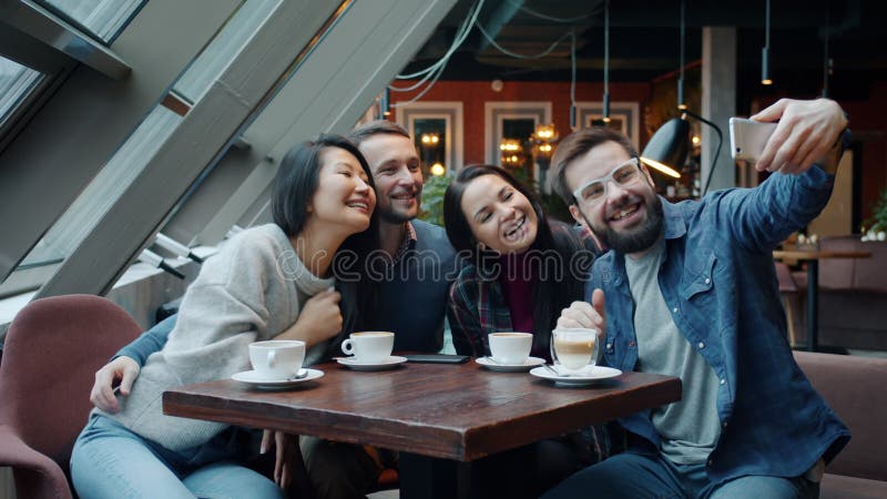 Grupo de jóvenes felices tomando selfie y divirtiéndose usando la cámara de un smartphone en el café