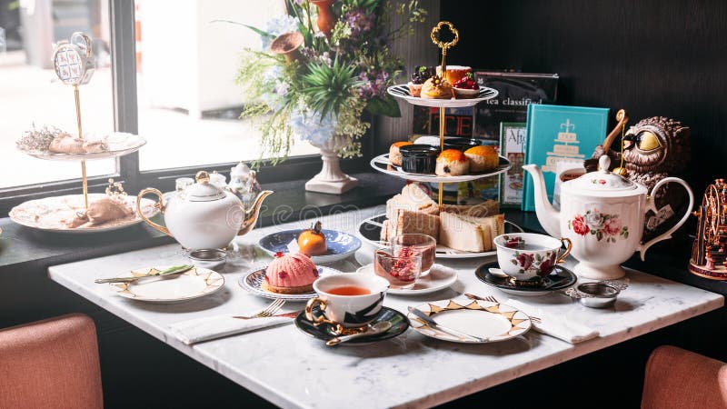 Grupo de lanche inglês que inclui o chá quente, a pastelaria, os bolos, os sanduíches e mini tortas na tabela superior de mármore