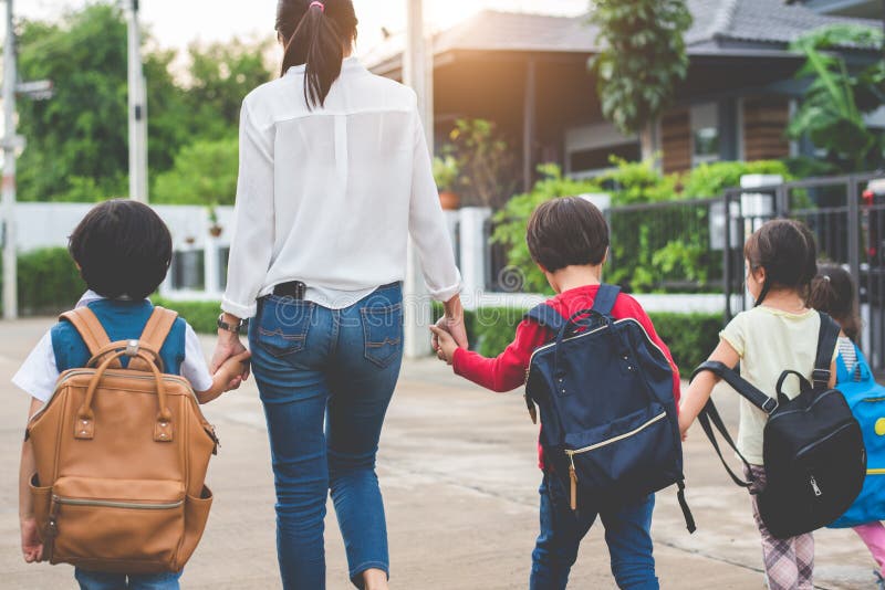 Grupo de madre y de ni? os que llevan a cabo las manos que van a ense? ar con la cartera La mamá trae a niños caminar a la escuela imagen de archivo libre de regalías