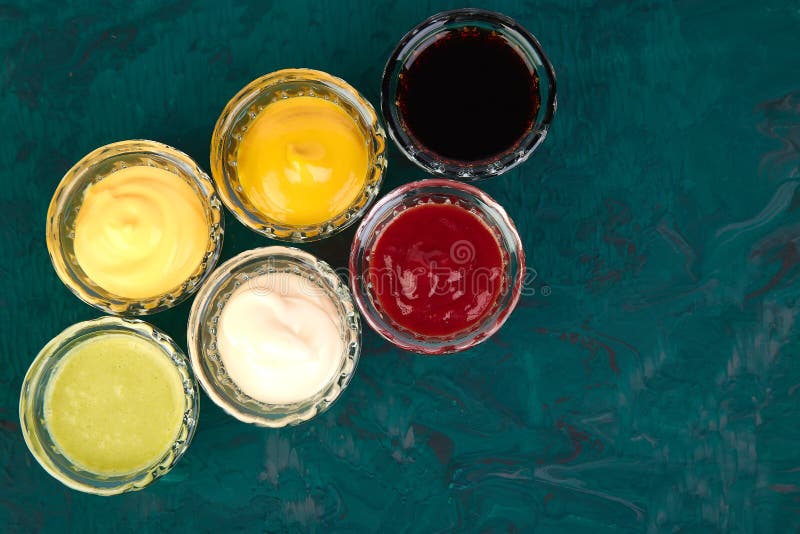 Set of different sauces. Sauces ketchup, mustard, mayonnaise, wasabi, soy sauce in little bowls on green background. Set of different sauces. Sauces ketchup, mustard, mayonnaise, wasabi, soy sauce in little bowls on green background