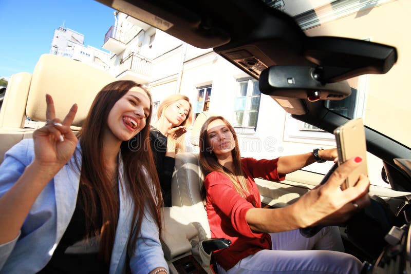 Grupo de muchachas que se divierten en el coche y que toman selfies con la cámara imágenes de archivo libres de regalías Grupo de muchachas que se divierten en el coche y que toman selfies con la cámara imágenes de archivo libres de regalías