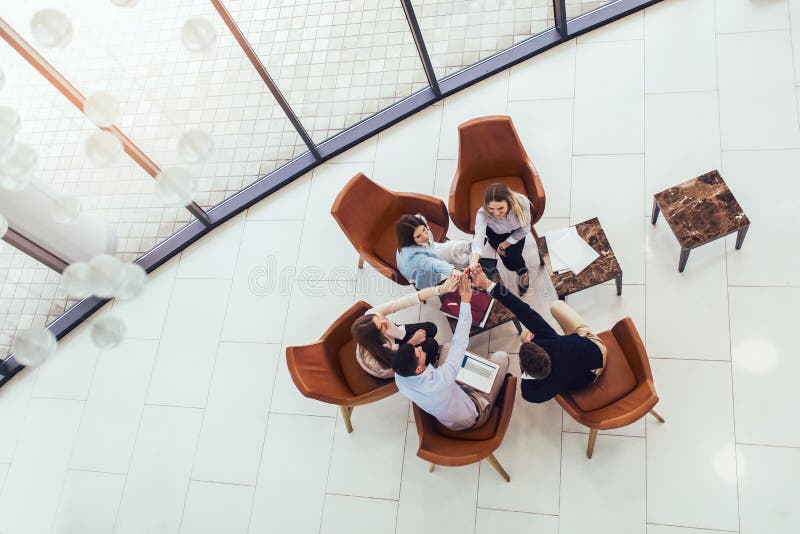 Grupo de profissionais novos do negócio que sentam-se junto e que têm a discussão ocasional no corredor do escritório Vista super imagem de stock Grupo de profissionais novos do negócio que sentam-se junto e que têm a discussão ocasional no corredor do escritório Vista super imagem de stock