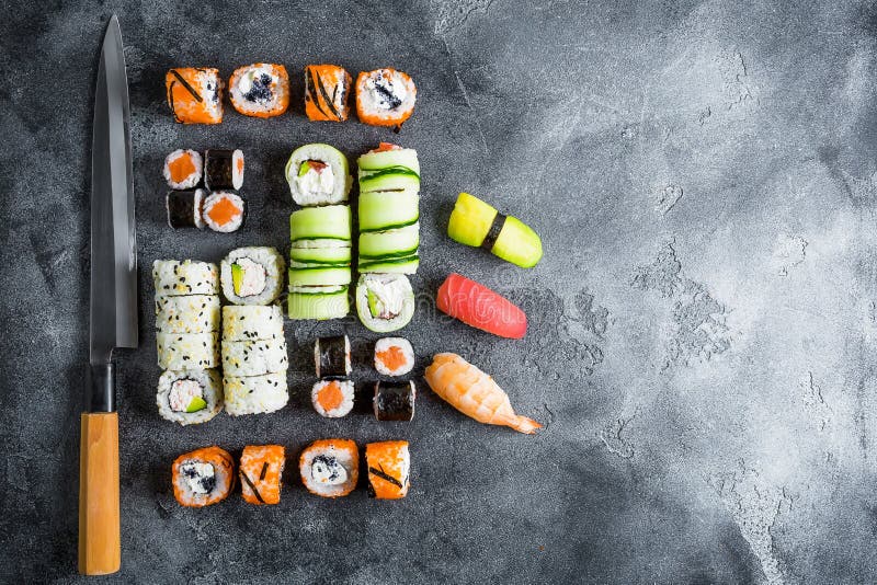 Grupo de rolos e de faca de sushi no fundo escuro Alimento japonês tradicional Copie o espaço Configuração lisa Vista superior foto de stock royalty free Grupo de rolos e de faca de sushi no fundo escuro Alimento japonês tradicional Copie o espaço Configuração lisa Vista superior foto de stock royalty free