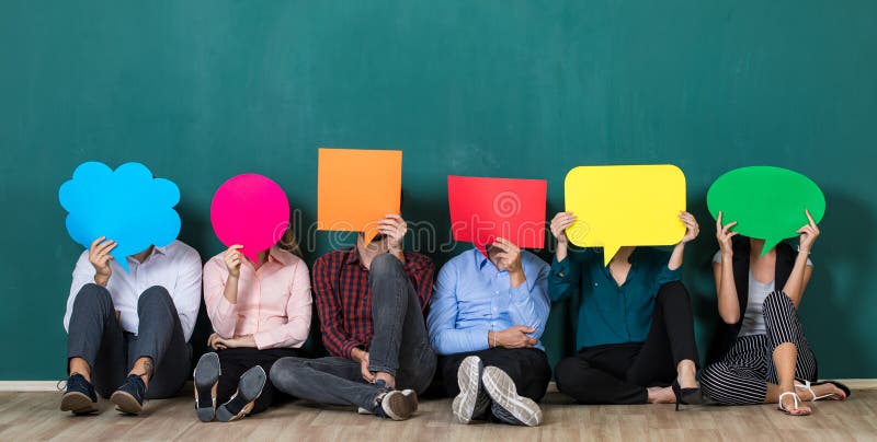 Group of six business people team sittiing together and holding colorful and different shapes of speech bubbles over their faces. Group of six business people team sittiing together and holding colorful and different shapes of speech bubbles over their faces.