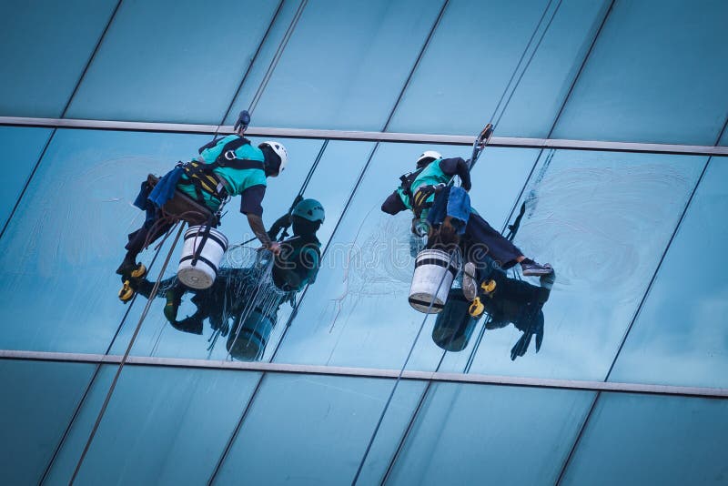 Grupo de trabalhadores que limpam o serviço das janelas na construção alta da elevação