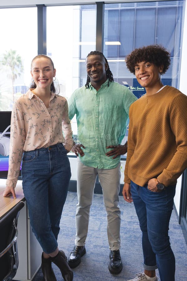 Diverse group of colleagues standing together, smiling, in a modern business office. Caucasian woman with blonde hair, African American and biracial men with dark hair, all wearing casual clothes, unaltered. Diverse group of colleagues standing together, smiling, in a modern business office. Caucasian woman with blonde hair, African American and biracial men with dark hair, all wearing casual clothes, unaltered
