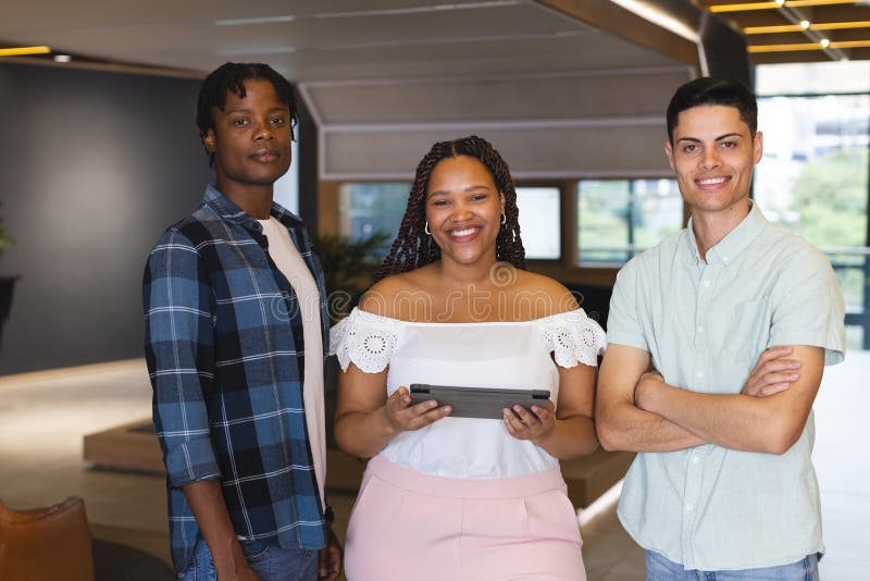 Diverse group of colleagues standing together in a modern business office, one holding tablet. African American men with short hair, biracial women with braids, and biracial men with neat haircut, all young, smiling, unaltered. Diverse group of colleagues standing together in a modern business office, one holding tablet. African American men with short hair, biracial women with braids, and biracial men with neat haircut, all young, smiling, unaltered.