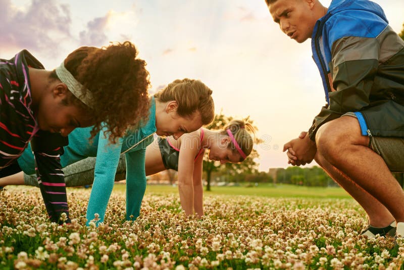 Grupo diverso de mujeres durante un entrenamiento de la aptitud que hace pectorales en la puesta del sol en parque de naturaleza fotografía de archivo libre de regalías Grupo diverso de mujeres durante un entrenamiento de la aptitud que hace pectorales en la puesta del sol en parque de naturaleza fotografía de archivo libre de regalías