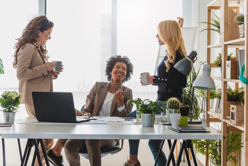 Grupo diverso de mujeres de negocios sonrientes que tienen una rotura en hablar de la oficina imagen de archivo libre de regalías