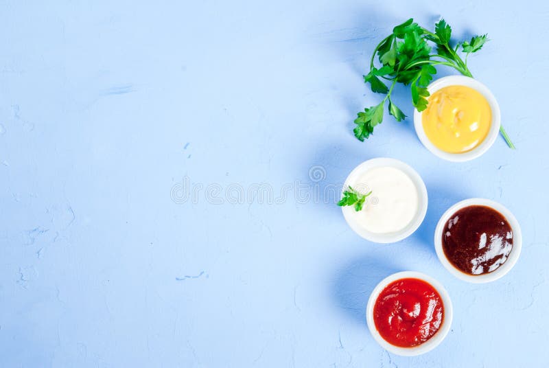 Classic set of sauces in white saucers: American yellow mustard, ketchup, barbecue sauce, mayonnaise. On the light blue stone concrete table top view, copy space. Classic set of sauces in white saucers: American yellow mustard, ketchup, barbecue sauce, mayonnaise. On the light blue stone concrete table top view, copy space