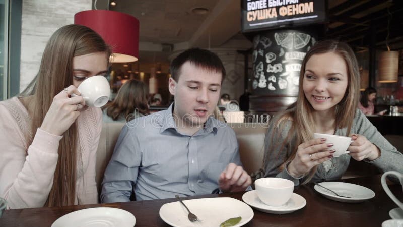 Grupo feliz de amigos duas jovens mulheres e um homem que conversa, tendo bebidas no café da cafetaria da cidade