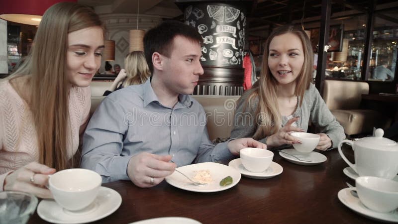 Grupo feliz de amigos duas jovens mulheres e um homem que conversa, tendo bebidas no café da cafetaria da cidade