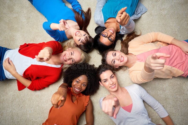 Diversity, race, ethnicity and people concept - international group of happy smiling different women lying on floor in circle and pointing finger at you. Diversity, race, ethnicity and people concept - international group of happy smiling different women lying on floor in circle and pointing finger at you