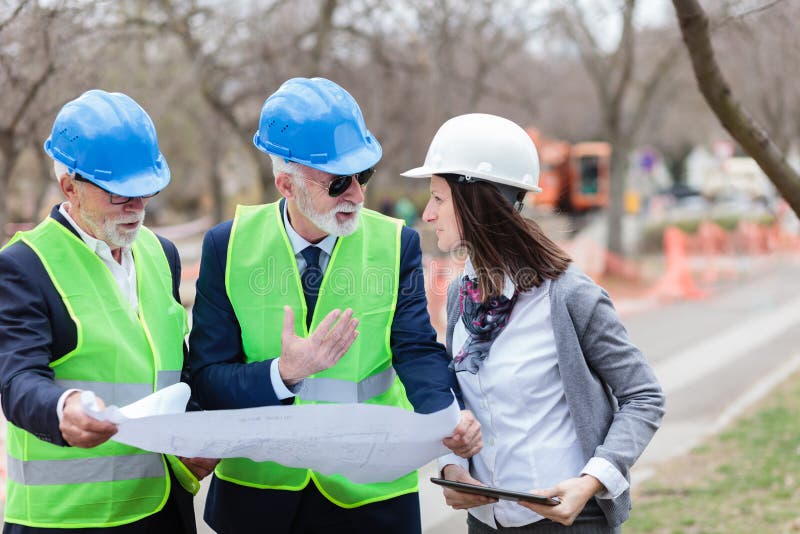 Grupo misturado de arquitetos e de sócios comerciais que discutem detalhes do projeto em um canteiro de obras fotografia de stock Grupo misturado de arquitetos e de sócios comerciais que discutem detalhes do projeto em um canteiro de obras fotografia de stock