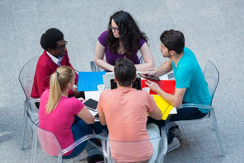 Grupo multirracial de estudiantes jovenes que estudian junto Tiro de alto ángulo de la gente joven que se sienta en la tabla fotos de archivo Grupo multirracial de estudiantes jovenes que estudian junto Tiro de alto ángulo de la gente joven que se sienta en la tabla fotos de archivo
