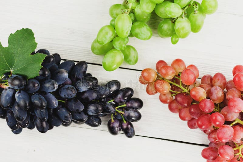 Grupos de uvas azuis e cor-de-rosa e verdes maduras frescas em pranchas brancas de madeira velhas imagens de stock Grupos de uvas azuis e cor-de-rosa e verdes maduras frescas em pranchas brancas de madeira velhas imagens de stock