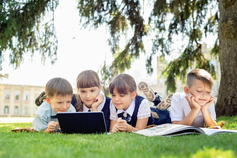 Grupp av elever i grundskolan som arbetar tillsammans med naturen i parken och gör läxor på den bärbara datorn arkivbilder