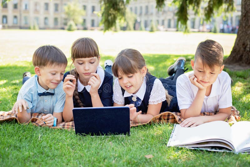 Grupp av elever i grundskolan som arbetar tillsammans med naturen i parken och gör läxor på den bärbara datorn arkivfoton