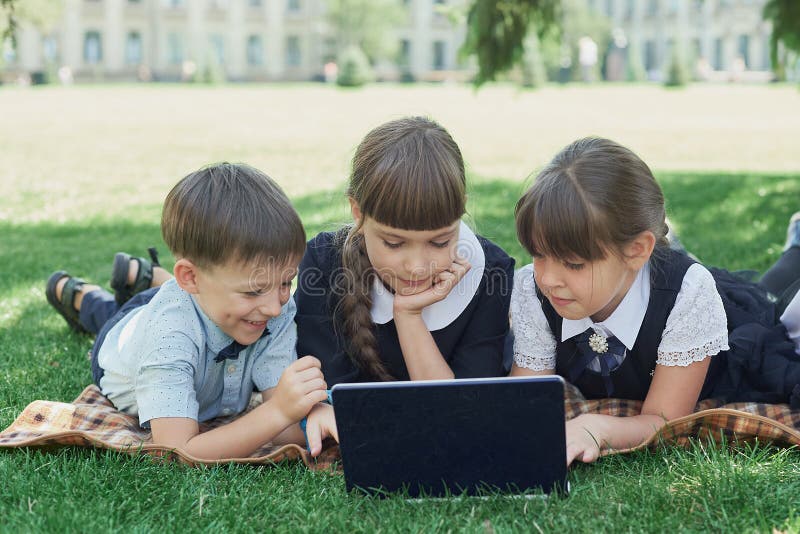 Grupp av elever i grundskolan som arbetar tillsammans med naturen i parken och gör läxor på den bärbara datorn royaltyfria foton