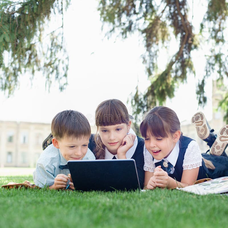 Grupp av elever i grundskolan som arbetar tillsammans med naturen i parken och gör läxor på den bärbara datorn royaltyfri bild