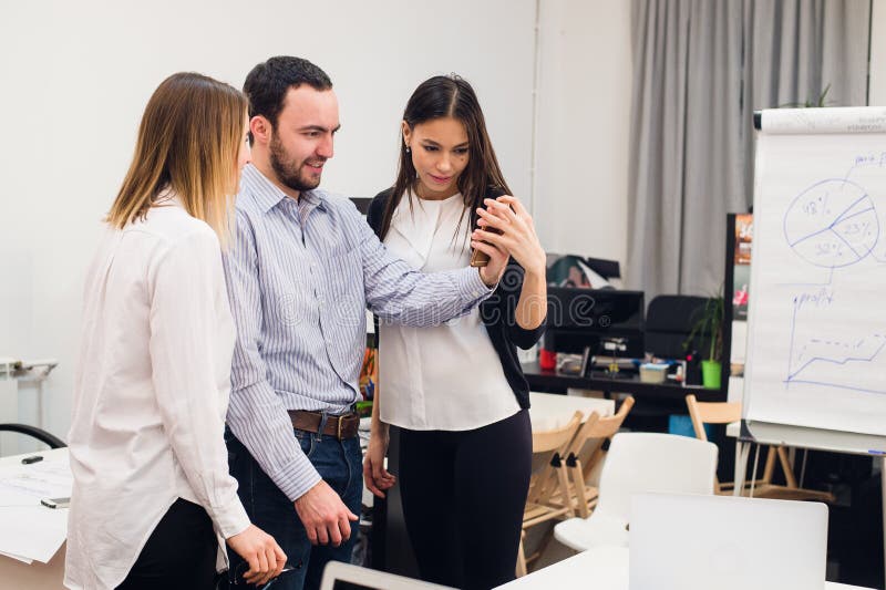 Grupp av fyra olika gladlynta medarbetare som tar självståenden och gör roliga gester med händer på det lilla kontoret arkivbilder Grupp av fyra olika gladlynta medarbetare som tar självståenden och gör roliga gester med händer på det lilla kontoret arkivbilder