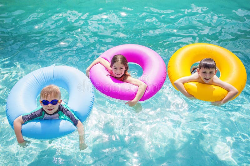 Group of cute kids playing on inflatable tubes in a swimming pool on a sunny day. Bright colorful fun summer photo with copy space. Group of cute kids playing on inflatable tubes in a swimming pool on a sunny day. Bright colorful fun summer photo with copy space