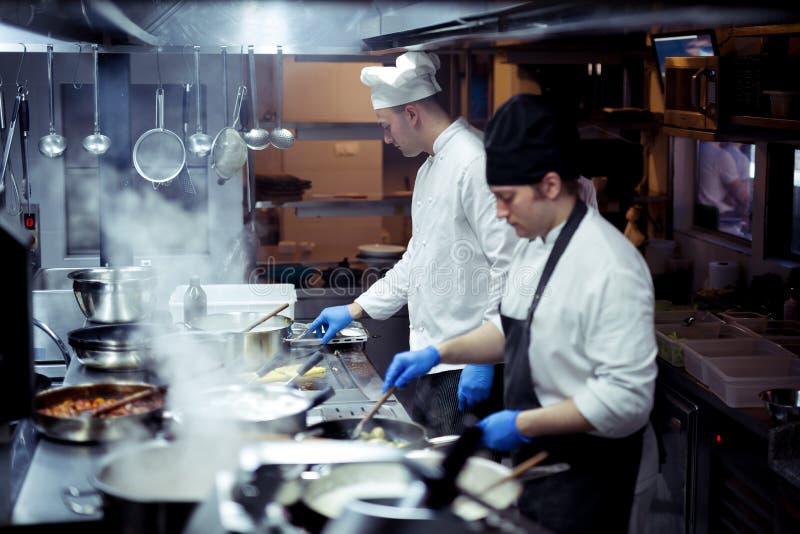 Grupp av kocken som förbereder mat i köket av en restaurang royaltyfri bild Grupp av kocken som förbereder mat i köket av en restaurang royaltyfri bild