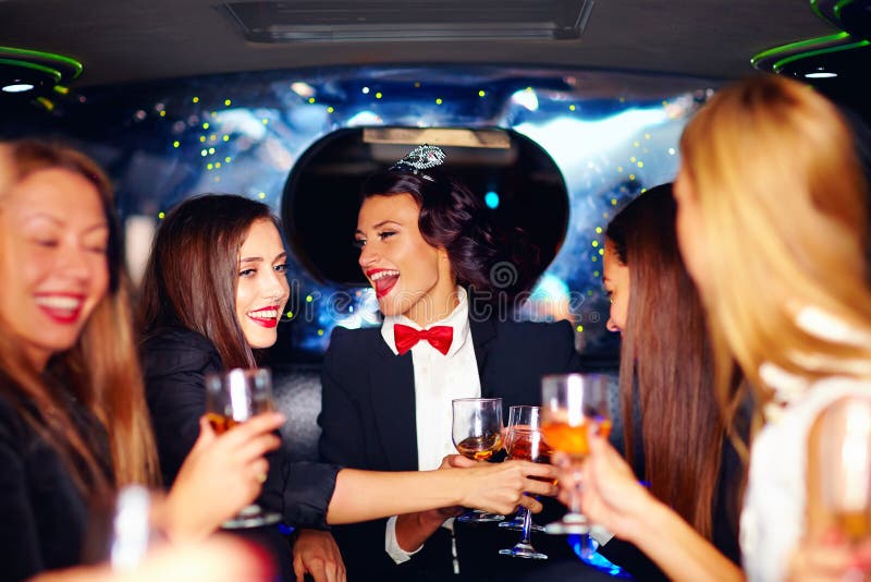 Grupp av lyckliga eleganta kvinnor som klirrar exponeringsglas i limousineet, möhippa royaltyfri fotografi