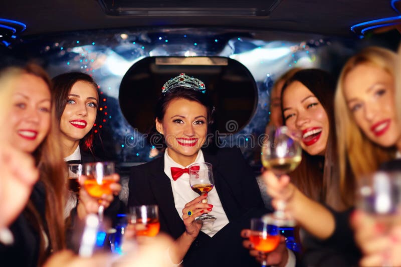 Grupp av lyckliga eleganta kvinnor som klirrar exponeringsglas i limousineet, möhippa royaltyfri foto