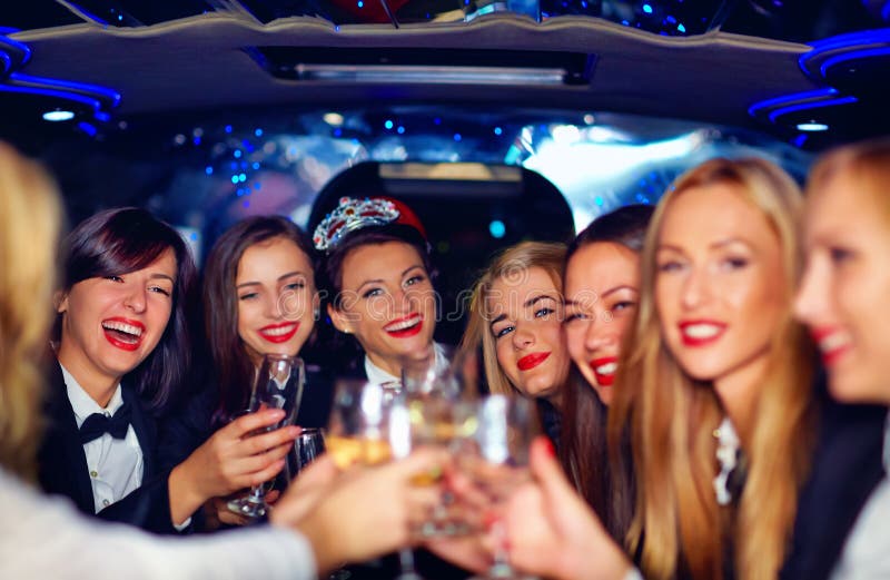 Grupp av lyckliga eleganta kvinnor som klirrar exponeringsglas i limousineet, möhippa arkivbild